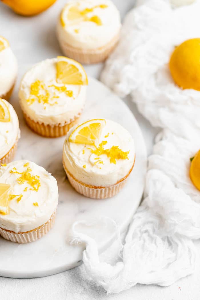 Delicious lemon cupcakes on white platter with a white flowy napkin and whole lemons in background