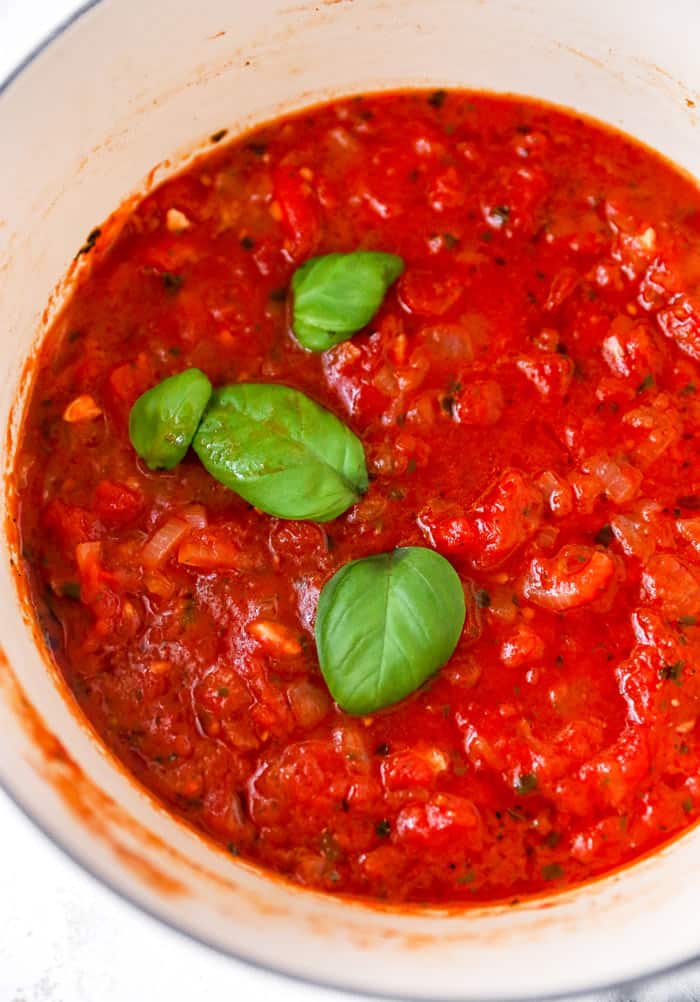 A sauteed marinara sauce in a large pot with fresh bay leaf