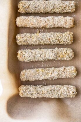 Breaded cheese sticks on parchment paper before frying