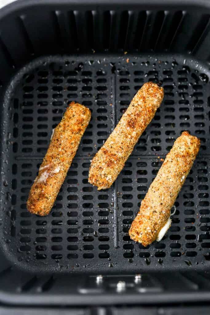 Three mozzarella cheese sticks in an air fryer basket