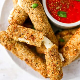 A delicious close up of mozzarella sticks on a white plate with one showing cheese pull