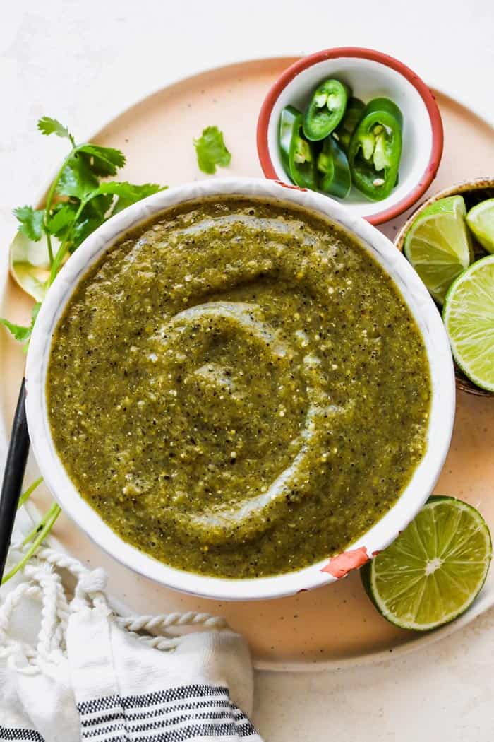 A white bowl filled with salsa verde, lime slices, cilantro around it