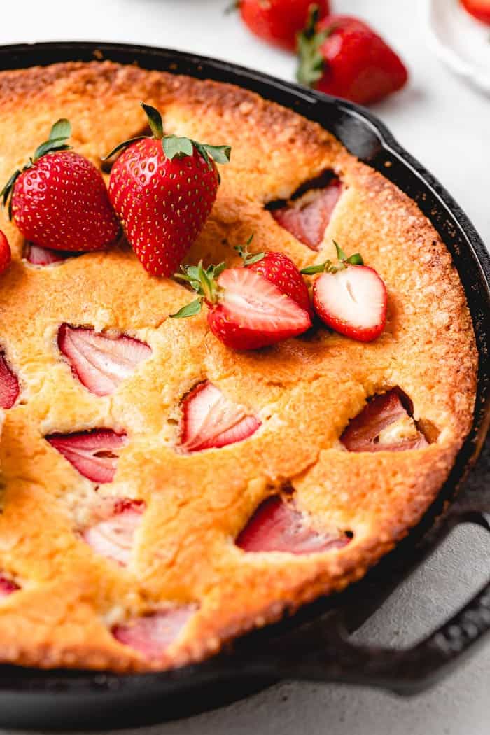 A close up of a strawberry cornmeal cake in a cast iron skillet with fresh berries on top