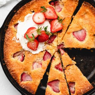 A delicious strawberry cornmeal cake in a cast iron skillet with slices cut and whipped cream on top