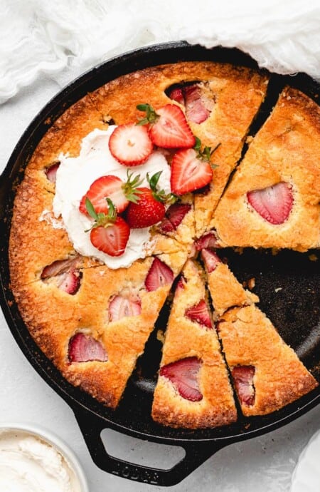 A delicious strawberry cornmeal cake in a cast iron skillet with slices cut and whipped cream on top