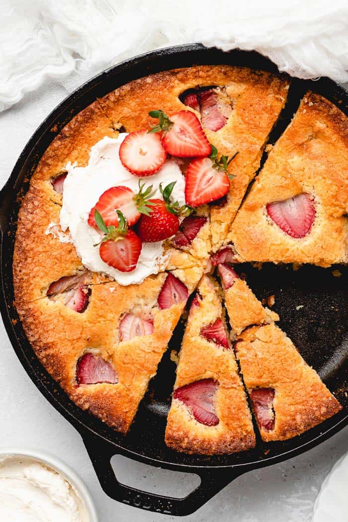 A delicious strawberry cornmeal cake in a cast iron skillet with slices cut and whipped cream on top