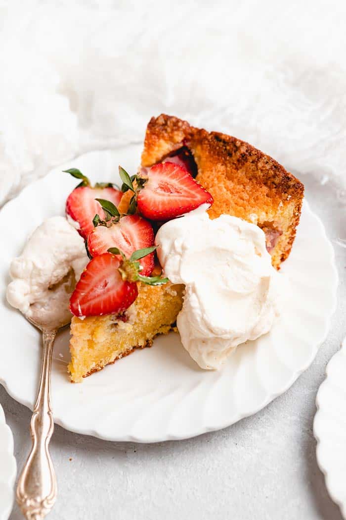 A slice of strawberry cake on a white plate with whipped cream and fresh strawberries
