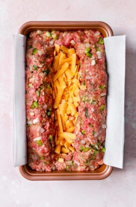 A meatloaf inside of a loaf pan with cheese stuffed in the center
