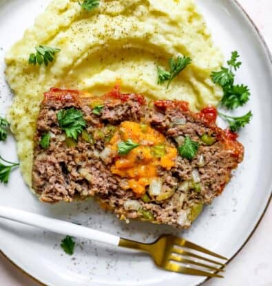 A slice of stuffed meatloaf on a white plate with mashed potatoes ready to enjoy