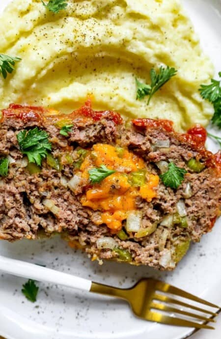 A slice of stuffed meatloaf on a white plate with mashed potatoes ready to enjoy