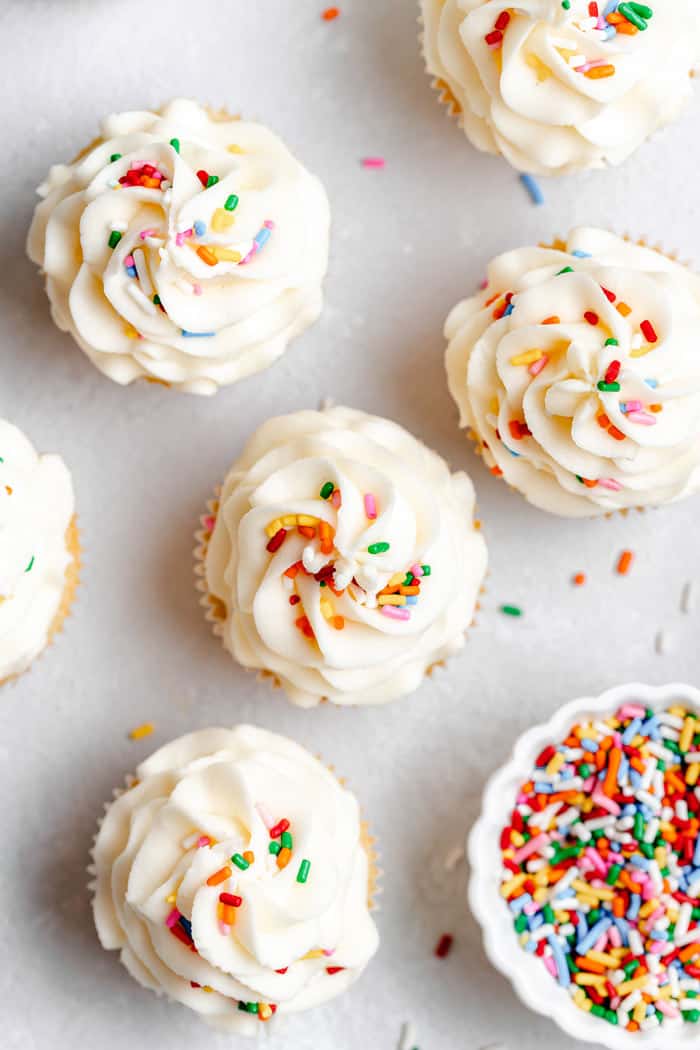 Perfectly frosted vanilla cupcakes with colorful sprinkles against gray background