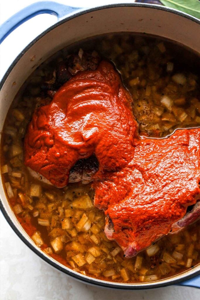 Chili paste being mixed into a pot of beef and broth.