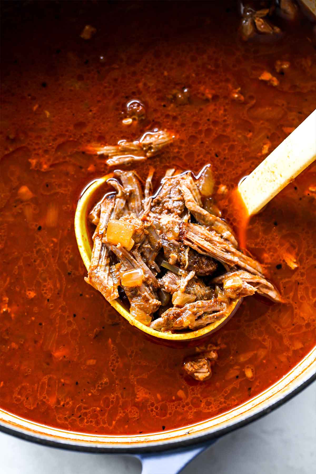 A pot of freshly made birria after being shredded with a large spoon coming out.