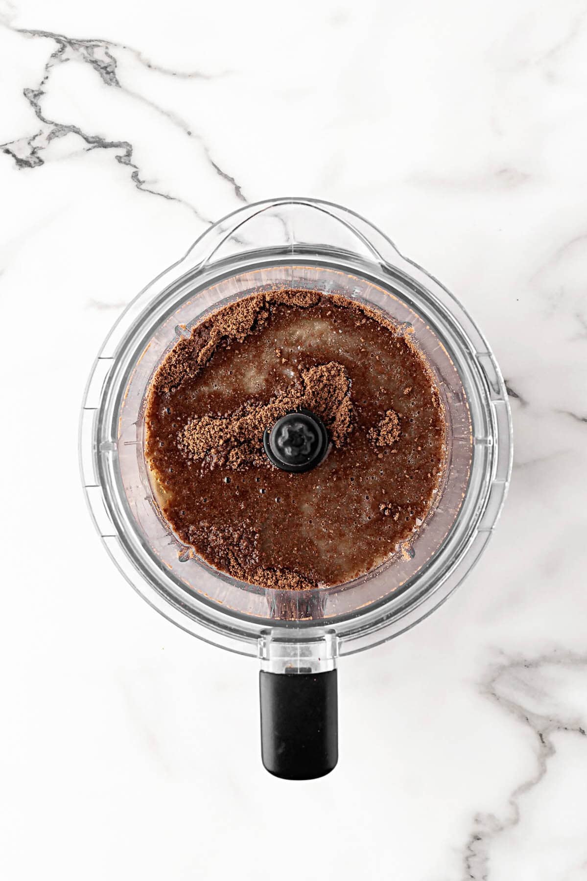 Overhead shot of crushed chocolate cookies and melted butter combined in a food processor for cheesecake crust