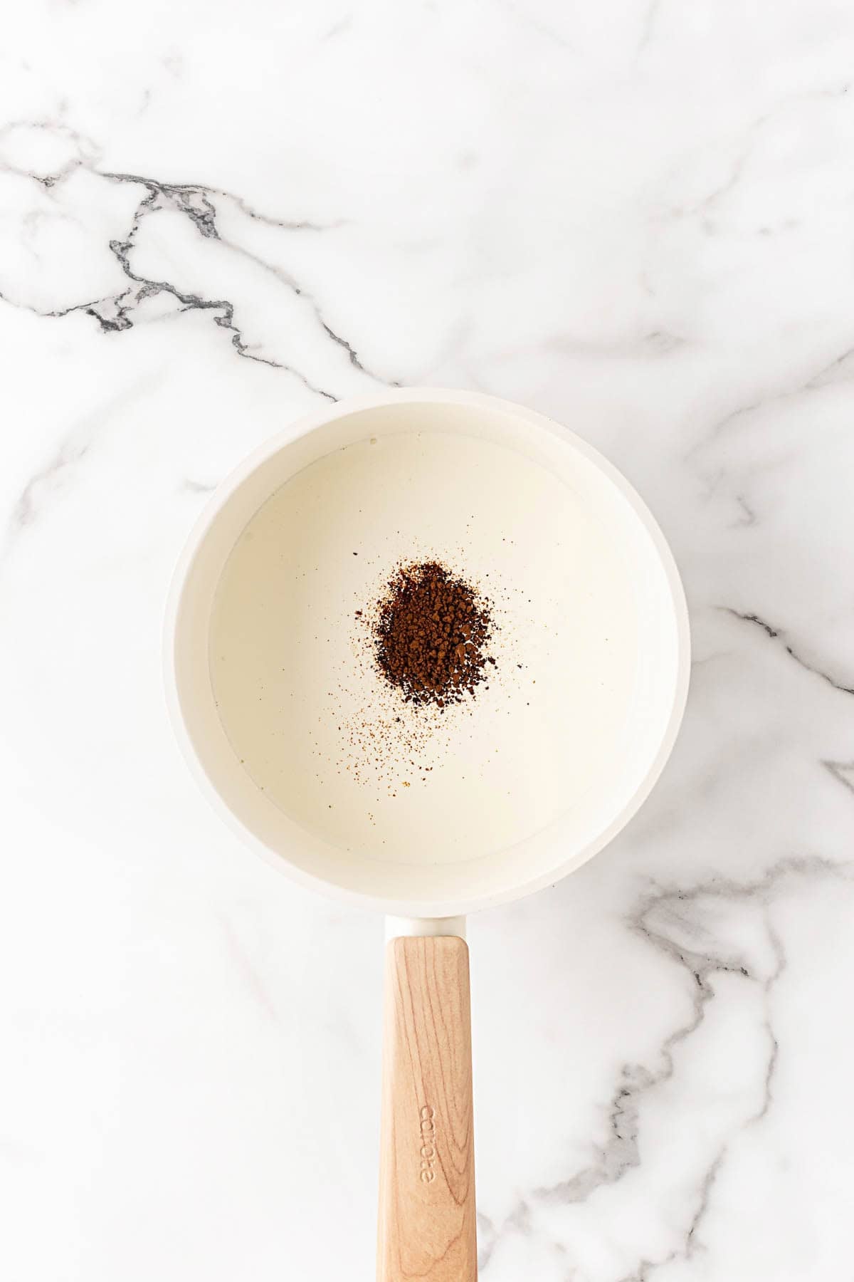 Heavy cream in a saucepan with coffee powder added on top before heating