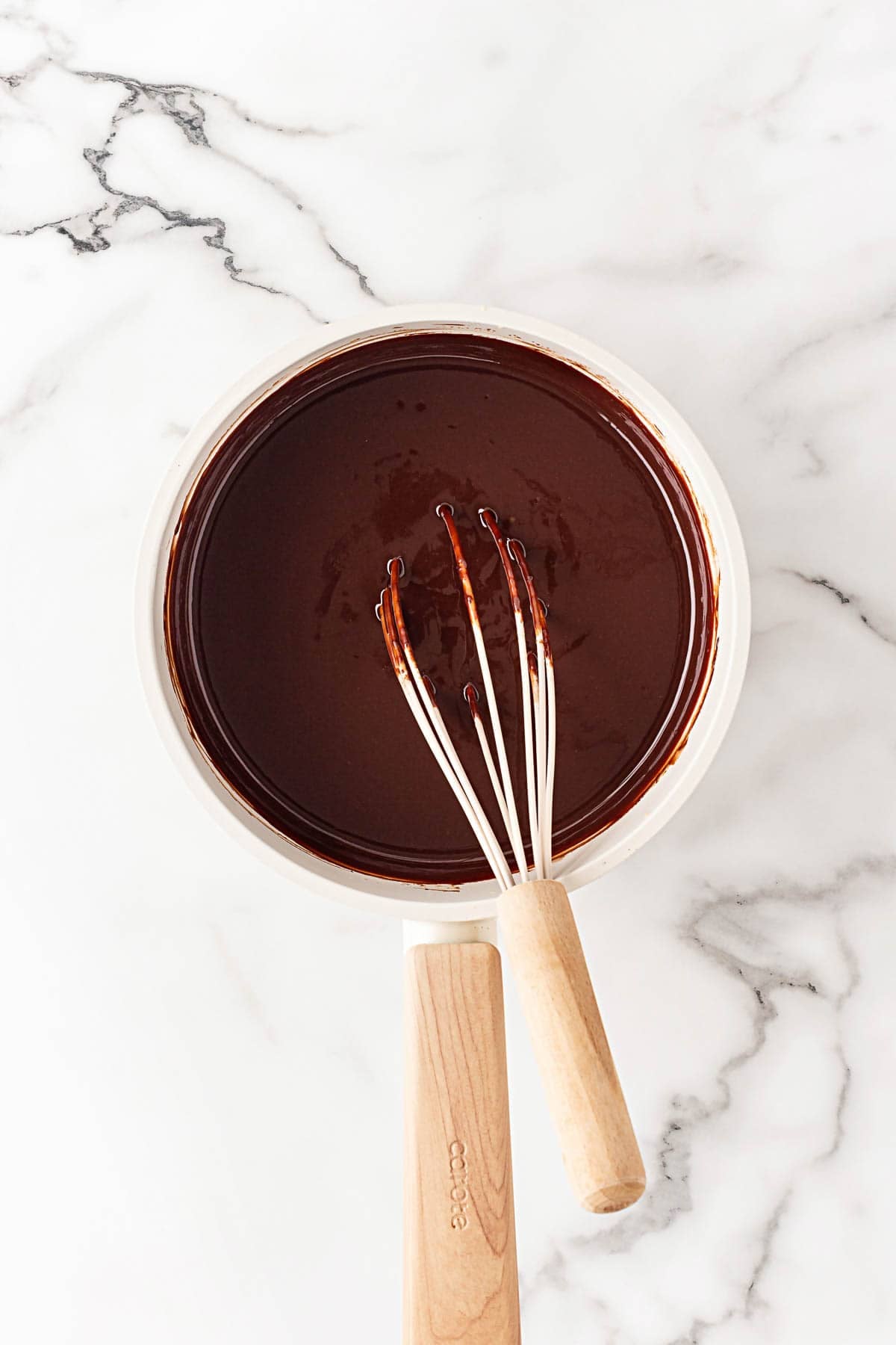 Smooth melted chocolate mixture in a saucepan with a whisk resting inside