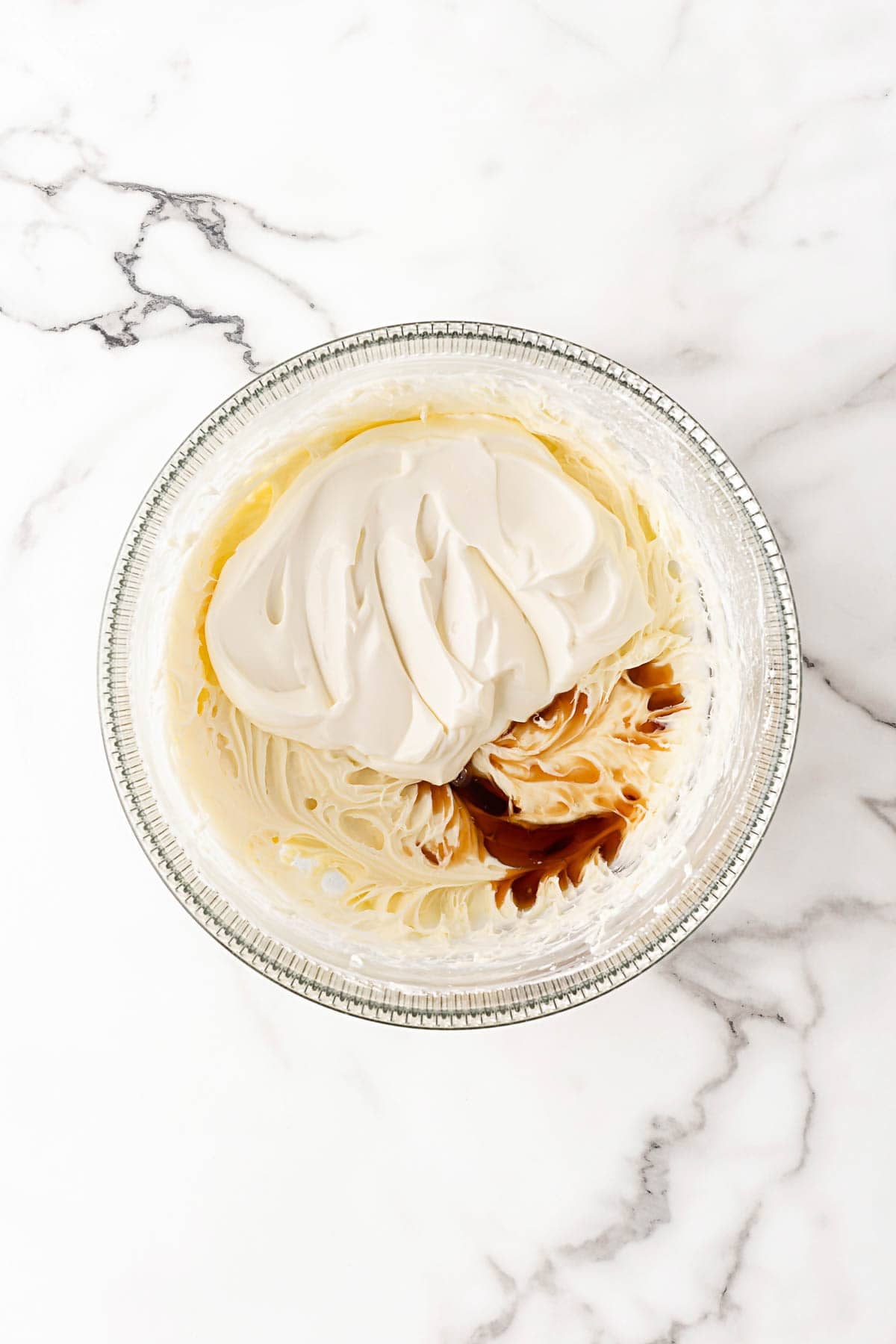 Cream cheese mixture in a glass bowl with sour cream and vanilla extract added on top