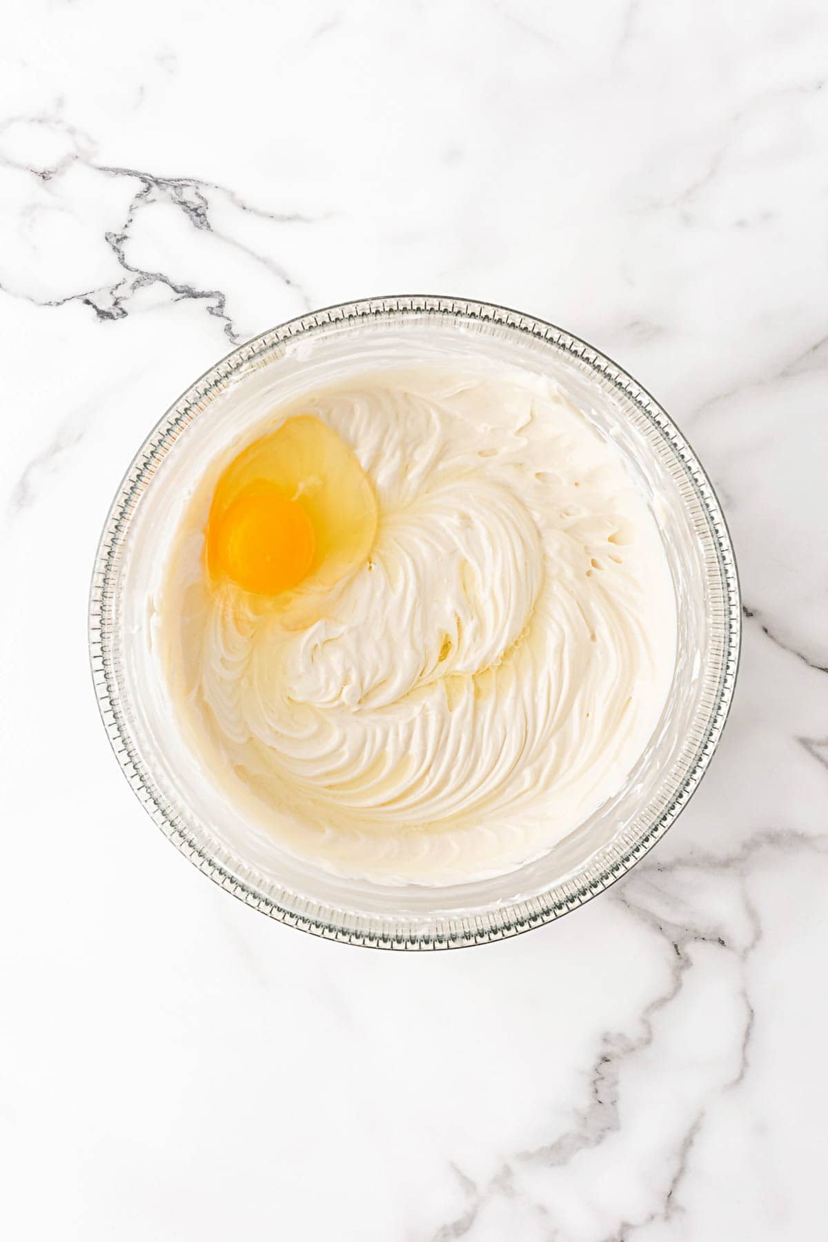 Cream cheese mixture in a bowl with an egg added before mixing