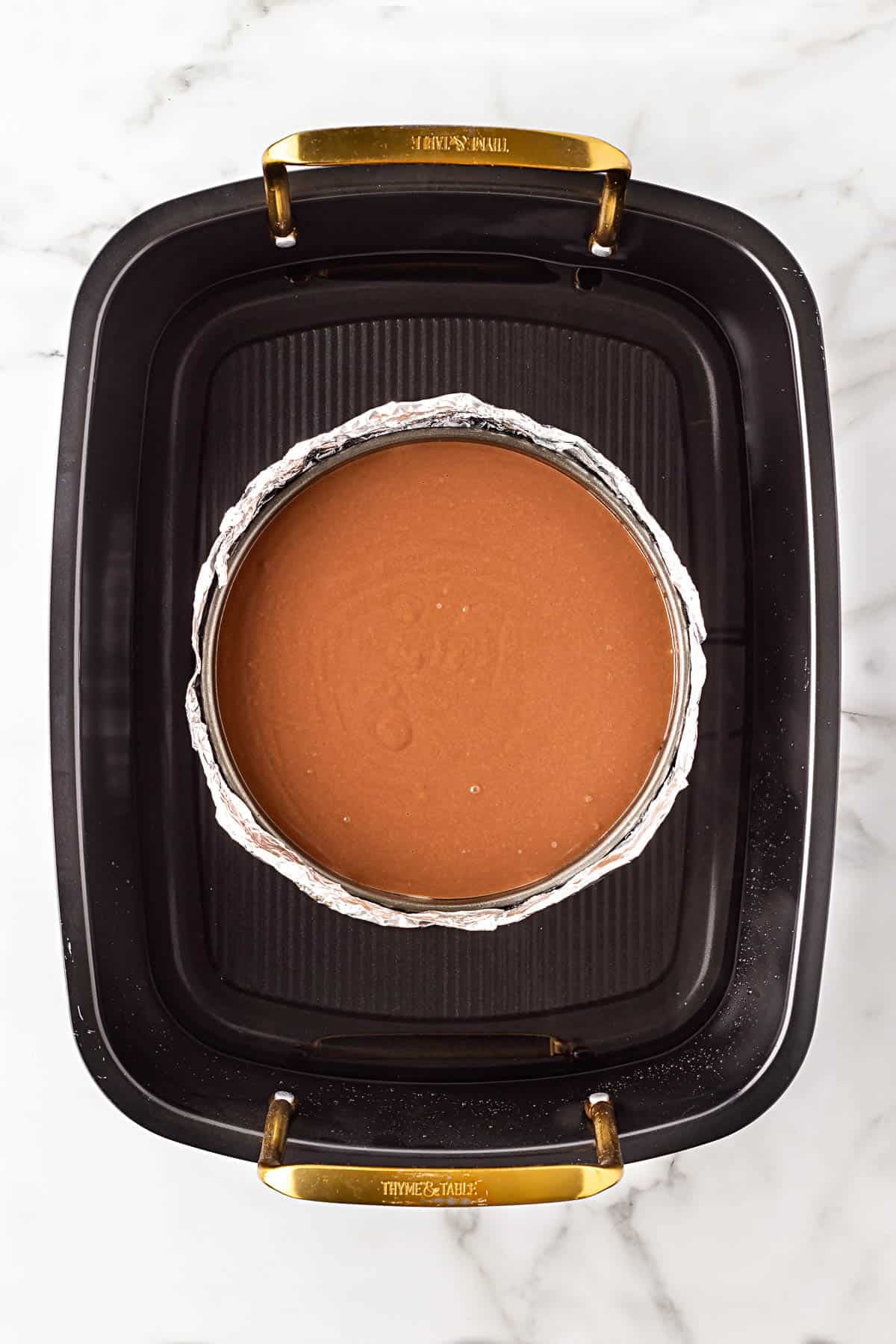 Chocolate cheesecake batter poured into a foil-wrapped springform pan inside a water bath