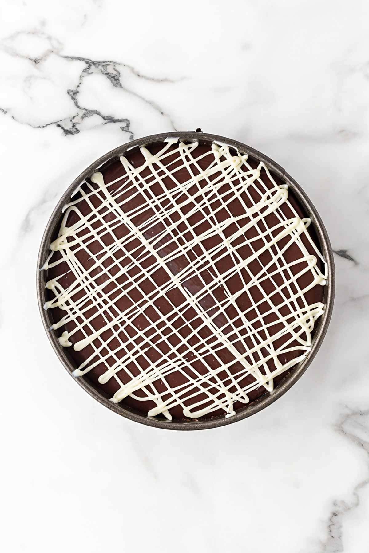 Chocolate cheesecake topped with white chocolate drizzle before chilling