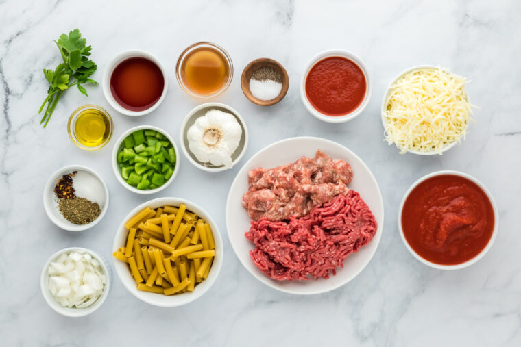 Sausage, turkey meat, cheese, pasta, sauce and veggies in bowls on a white background