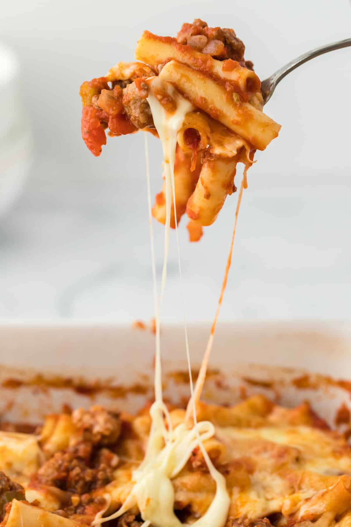 The Best Baked ziti recipe with a spoon lifting some out of baking dish