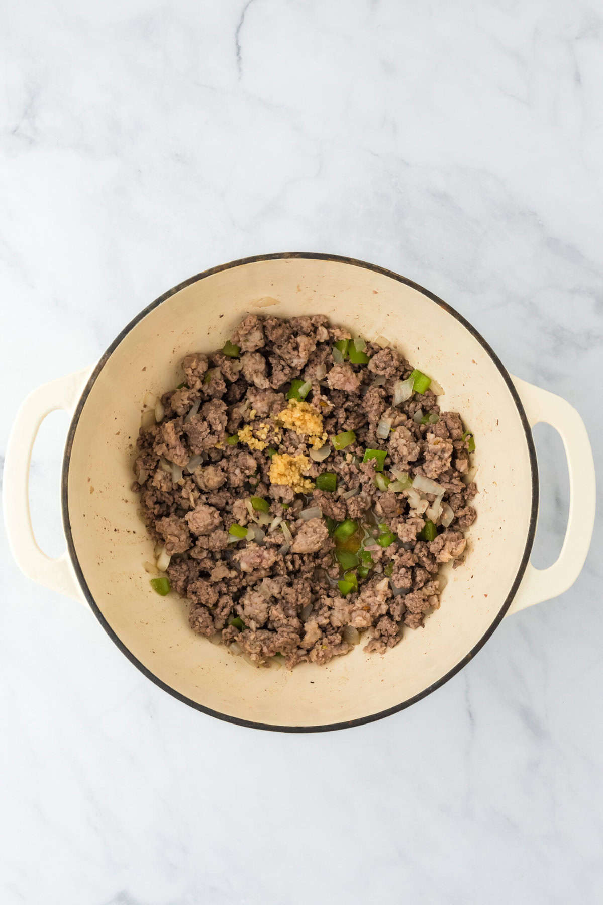 Browned meat in a large pot with garlic added as well on white background.