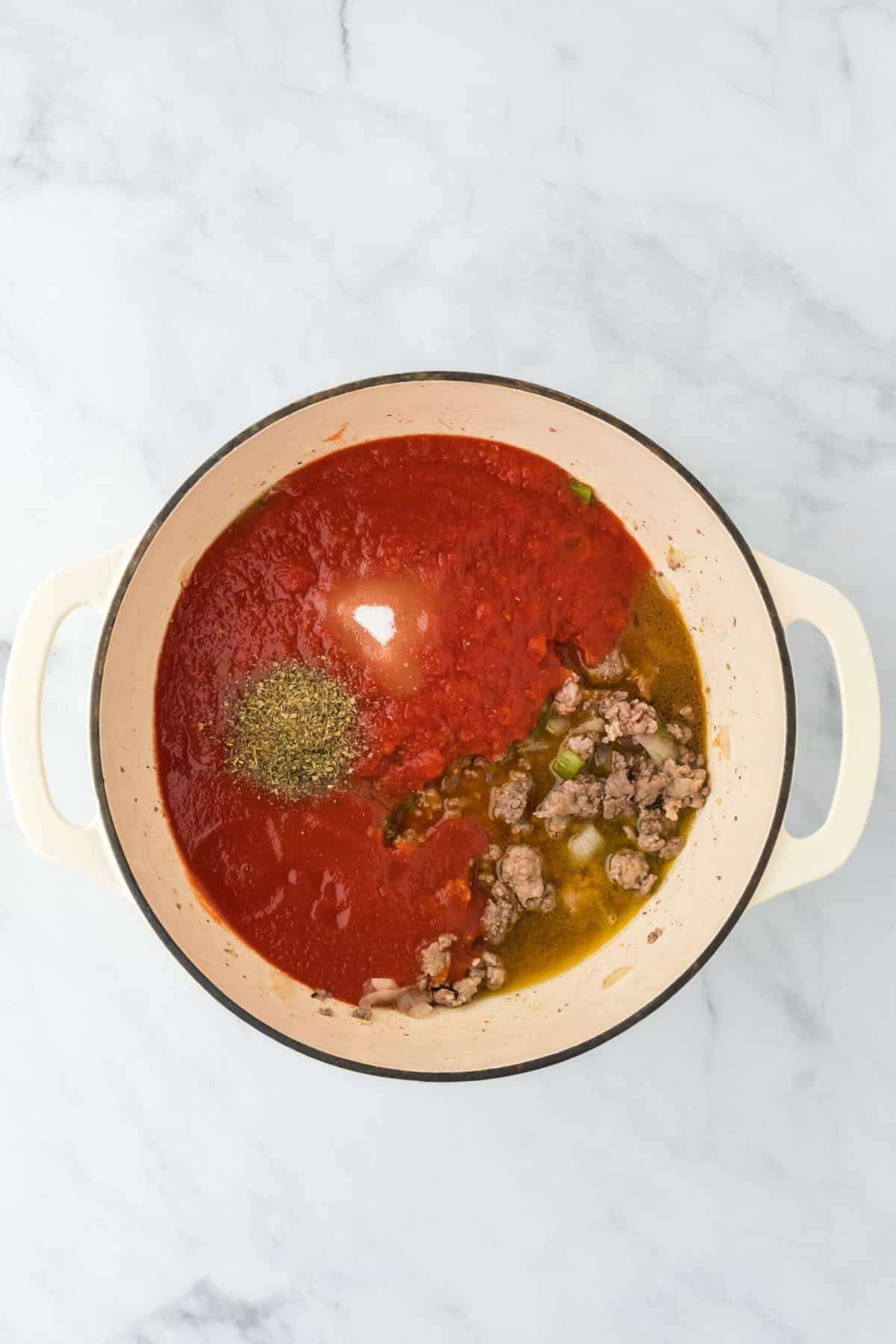 Crushed tomatoes and sauce ingredients being added to a large pot on white background