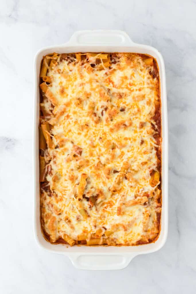 A golden browned baked ziti with sausage out of the oven on white background