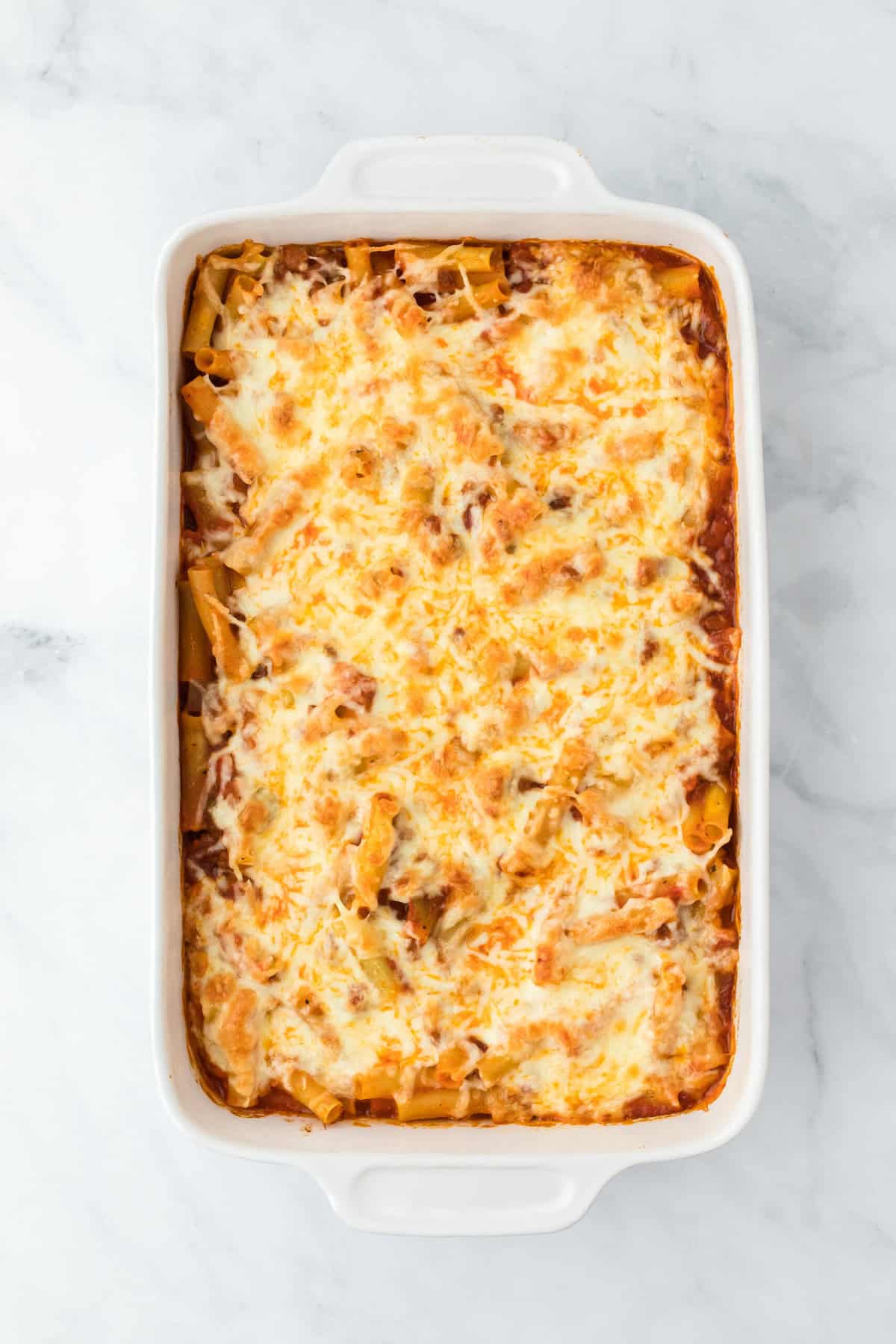 A golden browned baked ziti with sausage out of the oven on white background