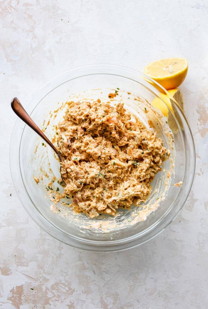 Crab stuffing in a clear bowl with a spoon and lemon wedges after being mixed