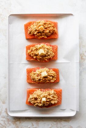 Filets of salmon on a baking sheet lined with parchment paper with crab stuffed and pats of butter before baking