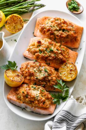 Cajun crab stuffed salmon on a white platter with lemon wedges and herbs ready to serve