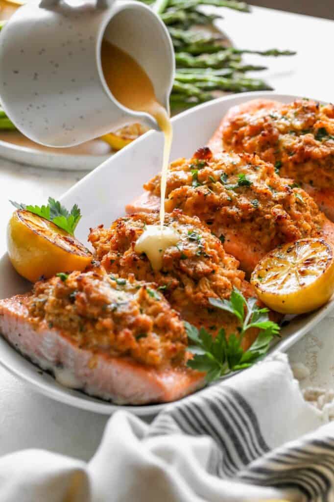 Crab stuffed fish recipe on a white platter with lemon sauce being poured on top in white background