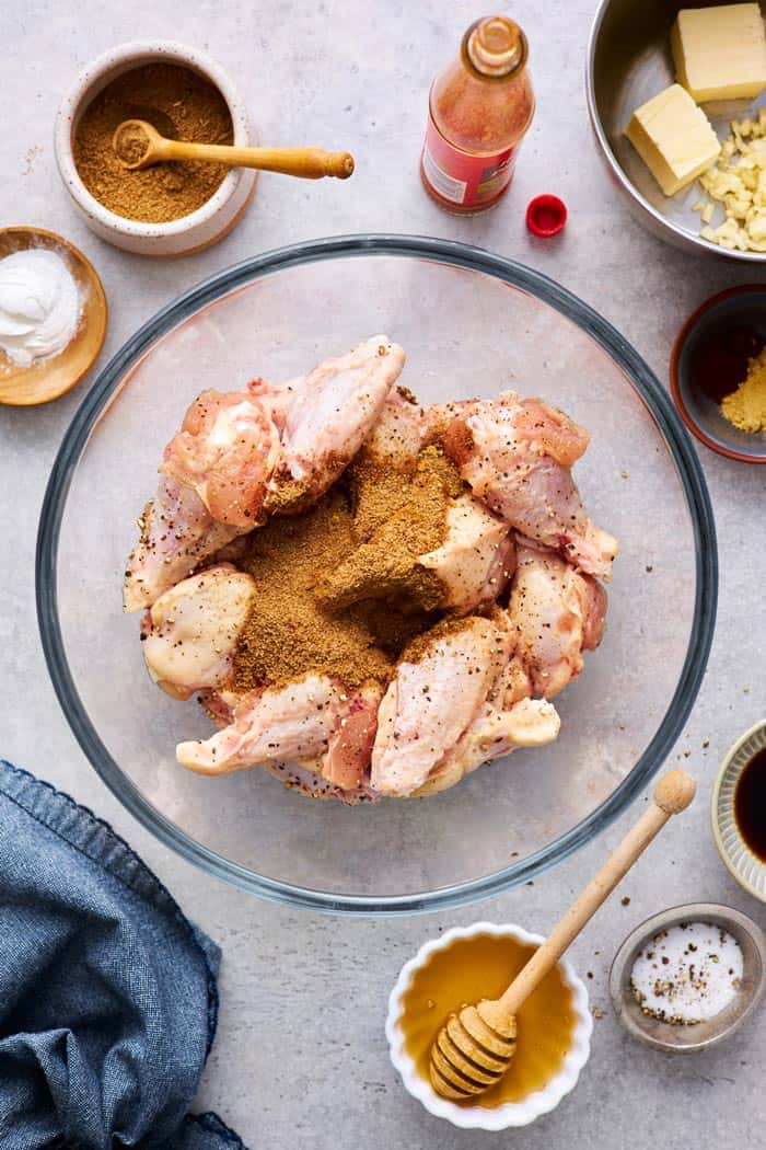 Party wings in a clear bowl with jerk seasoning on top ready to mix in