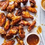 Jerk party wings coated in a honey garlic sauce scattered on parchment paper with glaze nearby