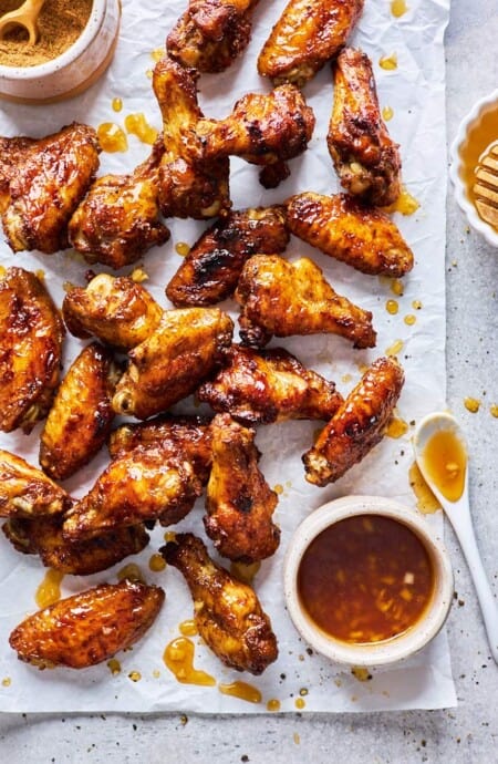Jerk party wings coated in a honey garlic sauce scattered on parchment paper with glaze nearby