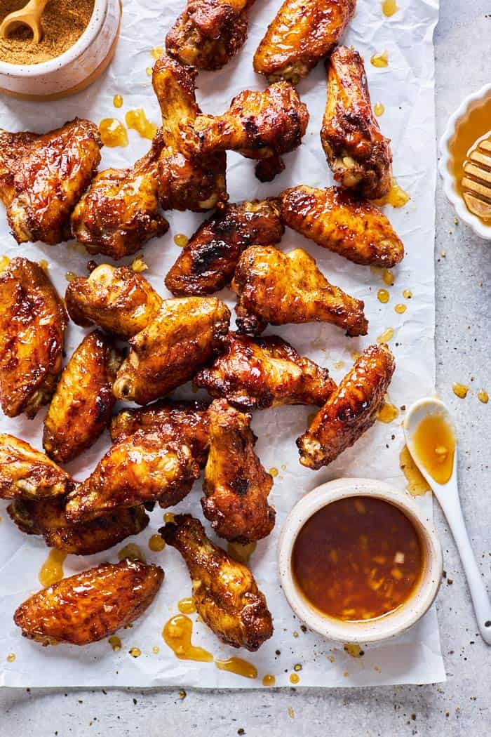 Jerk party wings coated in a honey garlic sauce scattered on parchment paper with glaze nearby