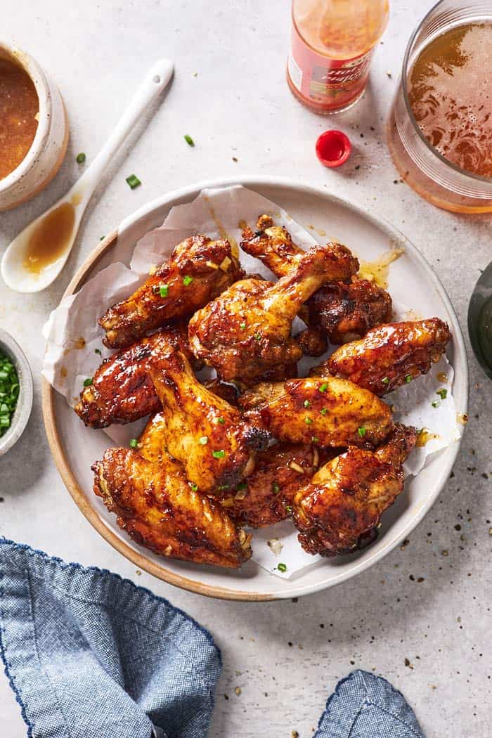 Jerk wings with honey garlic sauce glaze on a white plate with a blue towel and sauce behind it