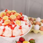 A delicious lemon strawberry pavlova ready to enjoy with lemons and strawberries surrounding it