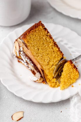 A close up of a slice of almond cake with a fork in the center being served