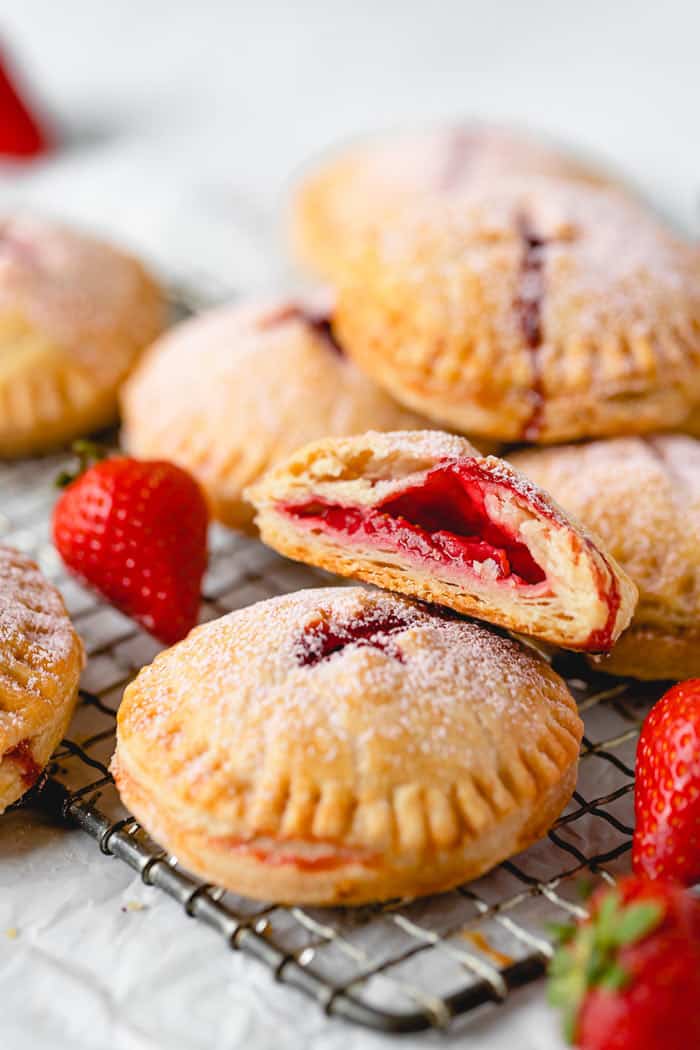 A close up of strawberry hand pies with one cut open showing strawberry filling