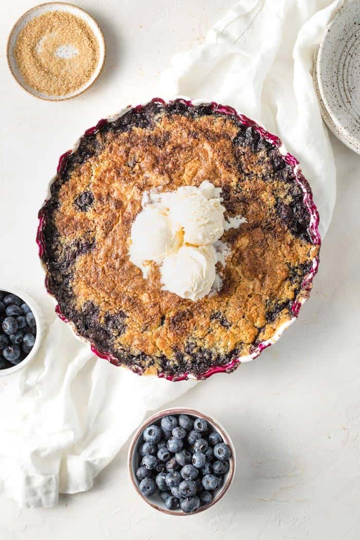 A deliciously easy blueberry cobbler baked with ice cream scoops on top on a white background