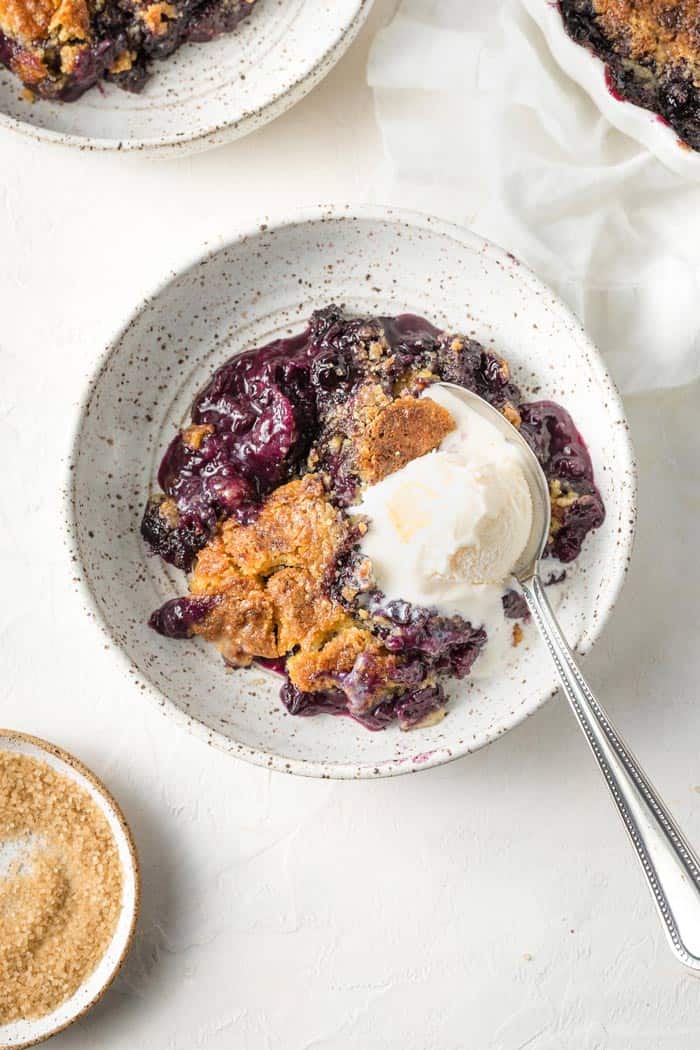 Southern Blueberry cobbler in a white bowl with melted vanilla ice cream on top