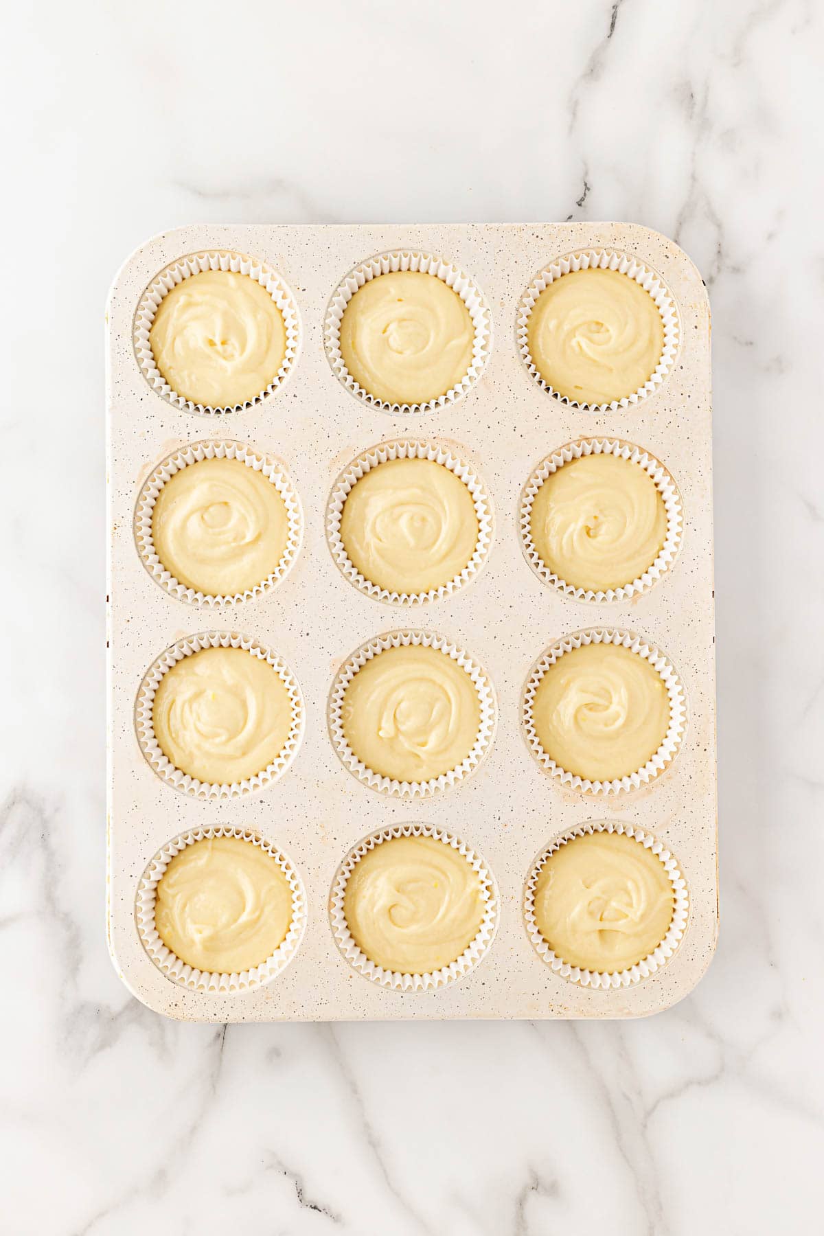 Unbaked cupcake batter evenly divided into a 12-cup muffin pan with white liners