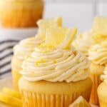 A plate full of frosted lemon cupcakes decorated with lemon wedges and zest
