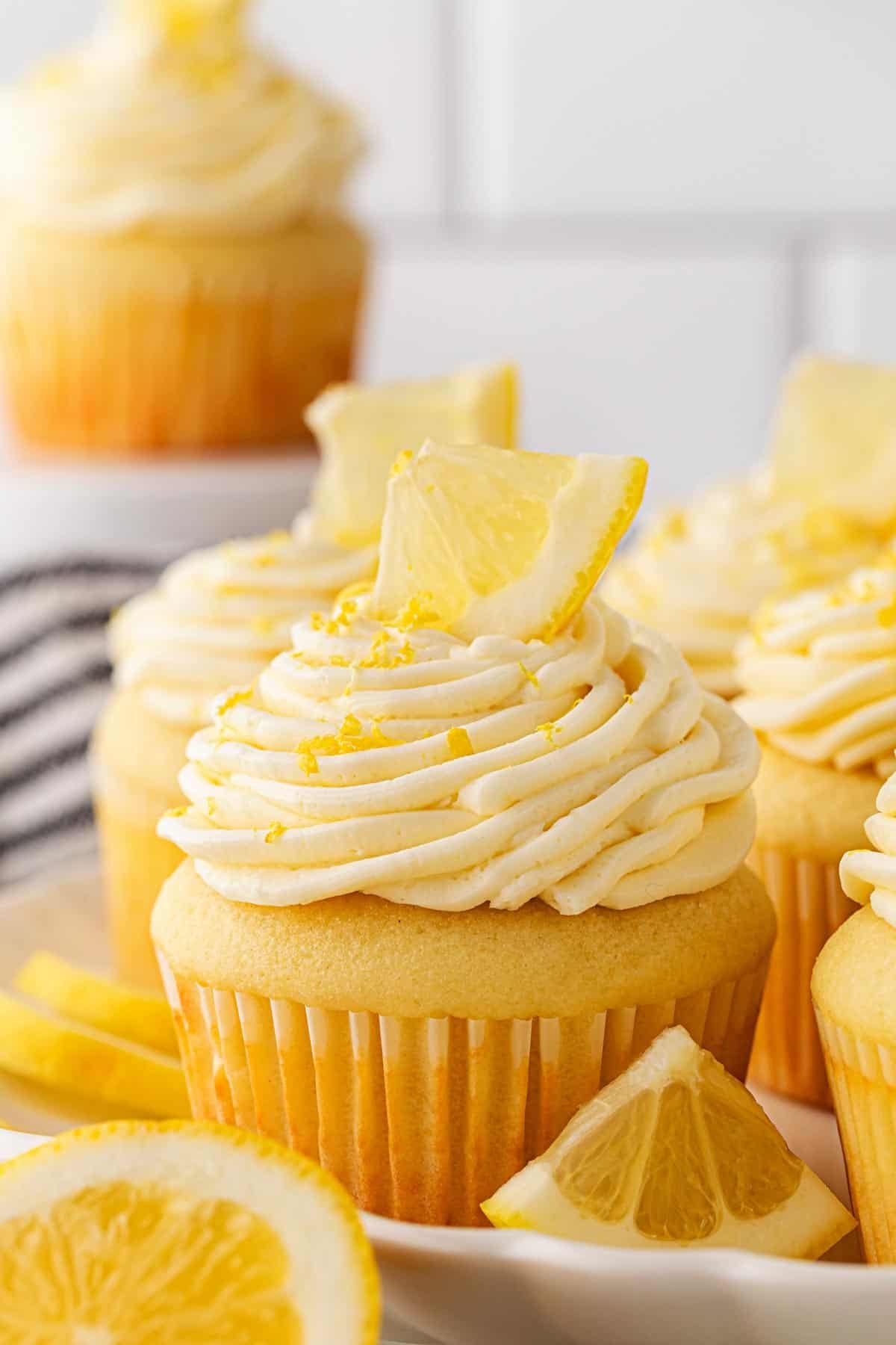 A plate full of frosted lemon cupcakes decorated with lemon wedges and zest