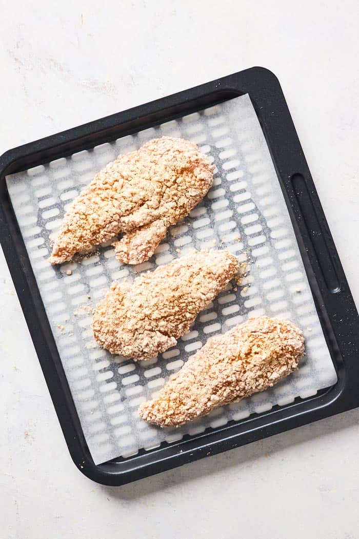 Breaded chicken tenders on a parchment paper lined tray for an air fryer