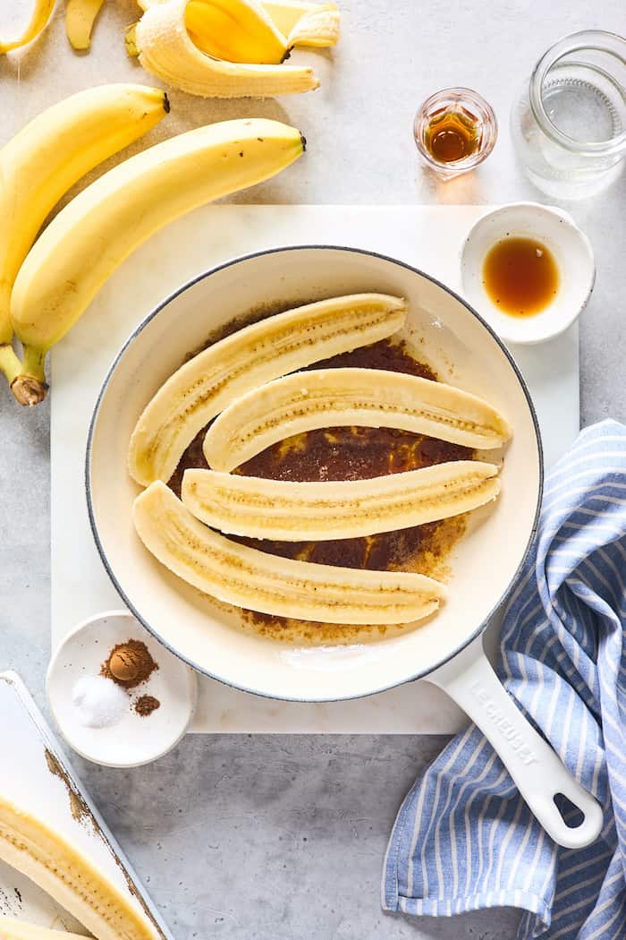 Fresh banana slices in a white skillet with sugar ready to flambe