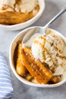 Flambeed bananas in two white bowls with vanilla ice cream scoops and sauce over the top
